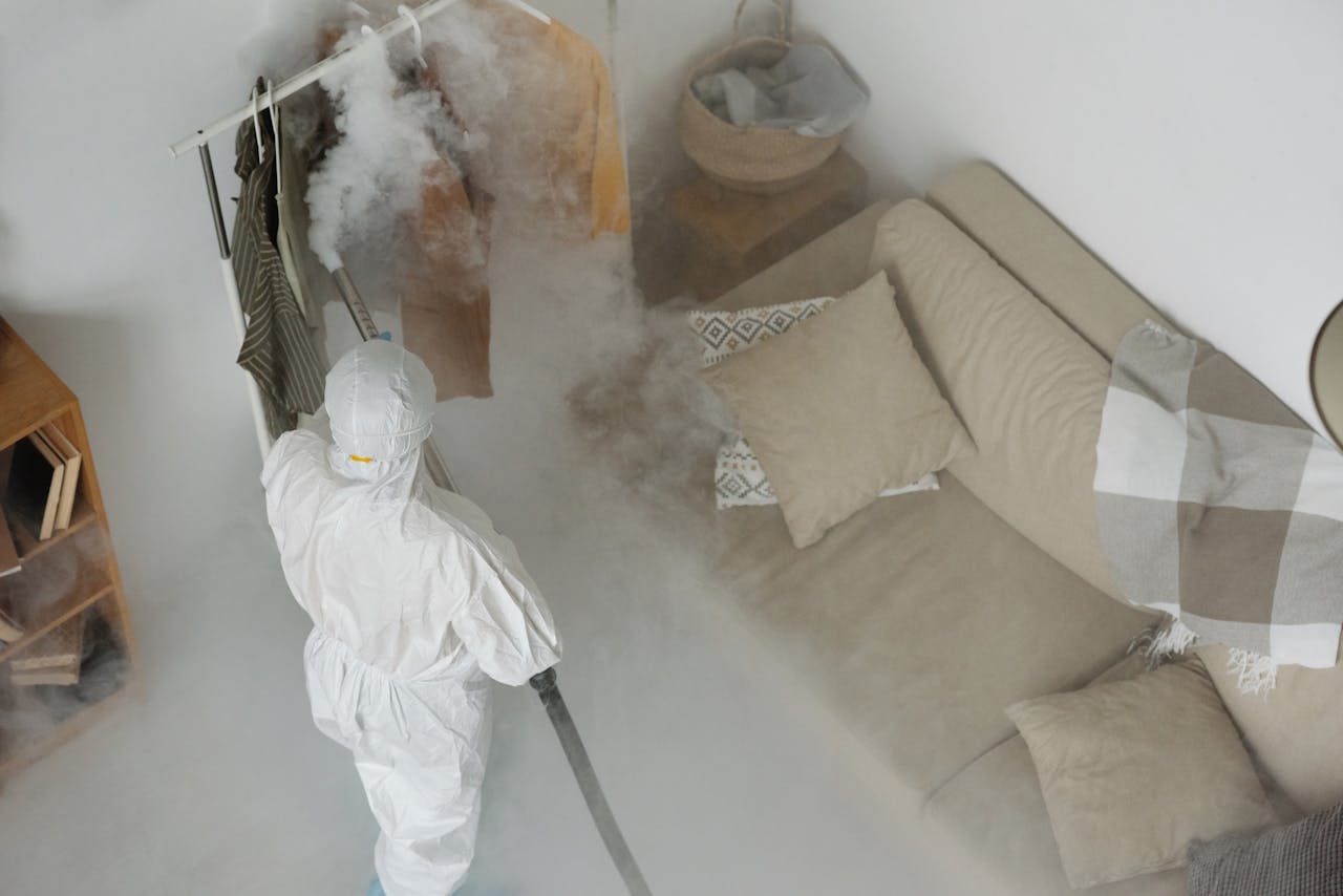services-02 A worker in protective gear performs fumigation in a living room, using smoke to sanitize surfaces.