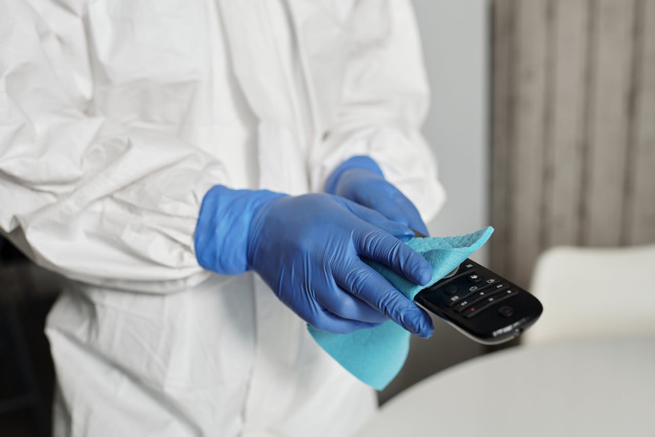 hero-img-01 Close-up of a person disinfecting a remote control wearing protective gloves, ensuring cleanliness.